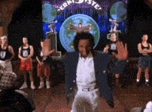 a man in a blue jacket and white pants is dancing on a stage in front of a crowd .