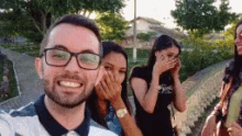 a man with glasses is taking a selfie with three women covering their faces .