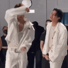 two men in white clothes are standing next to each other and one of them is holding a mirror .
