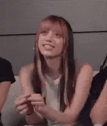a woman with pink hair is sitting on a couch smiling .