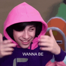 a young man wearing a pink hoodie and a purple sweatshirt is giving a thumbs up