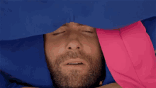 a man laying under a blue and pink blanket with his eyes closed