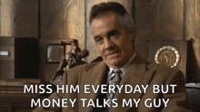 a man in a suit and tie is sitting in front of a wooden wall and talking about money .