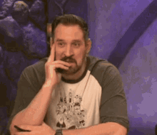 a man with a beard is sitting in front of a purple wall .