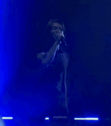 a man in a black shirt is singing into a microphone in a dark room ..