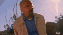 a man in a tan jacket is sitting on a rock .