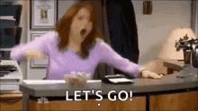 a woman in a purple sweater is sitting at a desk with her arms outstretched and a bowl of popcorn .