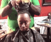 a woman is getting her hair done by a man in a green shirt and a black cape .