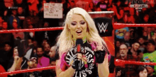 a woman in a wrestling ring is holding a microphone and smiling .