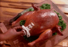 a person is tying a football shoe to a roasted chicken on a cutting board .