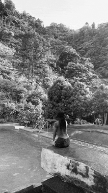 a woman is sitting on the edge of a swimming pool looking at the trees .