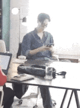a man is sitting at a desk in an office looking at his cell phone .