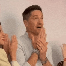 a man in a white shirt is clapping his hands in a room with other people .