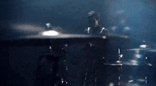 a man is playing drums in a dark room with smoke coming out of the drum set .