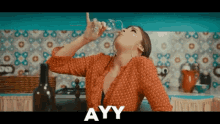 a woman is drinking from a glass with ayy written in the corner