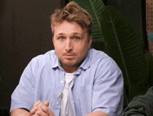 a man in a blue shirt with a pen in his pocket looks at the camera