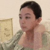 a woman in a green dress is sitting in front of a dresser and adjusting her hair .