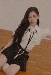 a woman in a white crop top and black pleated skirt is laying on the floor