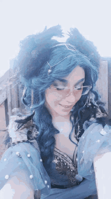 a woman with blue hair and glasses is wearing a crown of feathers