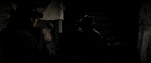 a man in a cowboy hat is standing in a doorway of a log cabin smoking a cigarette .