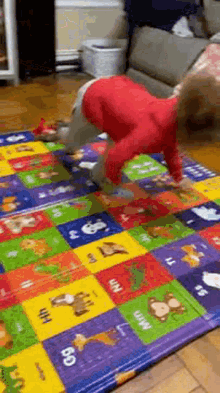 a baby is doing a handstand on a colorful play mat with letters and animals on it