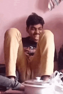 a man is sitting on the floor with his legs crossed and a pot in the background .
