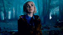 a woman is standing in the middle of a forest looking up at the sky .