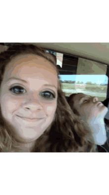 a woman taking a selfie in a car with another woman behind her