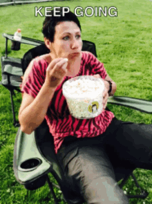 a woman is sitting in a chair eating a bowl of popcorn
