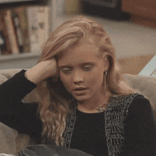 a young woman sitting on a couch with her hand on her head