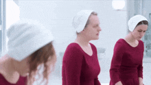 three women wearing red dresses and white hats stand in a room