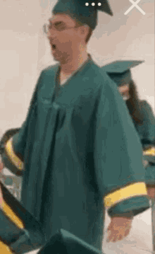 a man in a graduation cap and gown is standing in front of a table with his arms outstretched .
