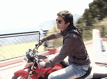 a man wearing sunglasses is riding a red motorcycle with a license plate that starts with the letter r