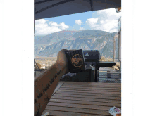 a person sitting on a wooden deck with mountains in the background and a mug that says ' ea ' on it