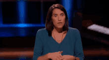 a woman in a blue shirt is sitting on a stage with her hands folded in front of her .