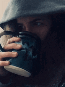 a person is drinking from a blue mug with a skull on it