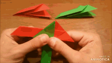 a person is holding a red and green origami object with the words made in animotica on the bottom
