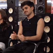 a man wearing a black tank top is sitting in front of a stack of speakers