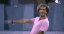 a man in a pink shirt is dancing with his arms outstretched in a room .