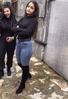 two women standing next to each other one wearing a black top and blue jeans