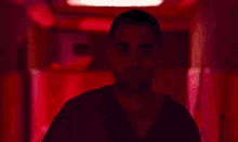 a man with a shaved head is standing in a red room in a hospital gown .
