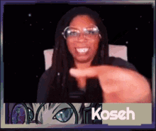 a woman wearing glasses is smiling and pointing at the camera with a koseh logo in the background