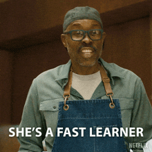 a man wearing glasses and an apron says " she 's a fast learner "