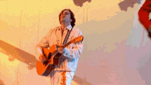 a man in a white jacket is playing an orange guitar on a stage