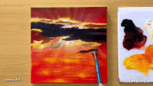 a painting of a sunset is being painted on a canvas by joony art