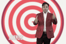a man in a red jacket stands in front of a red and white target that says dinngg on the bottom