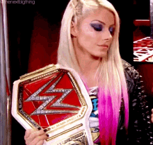 a blonde woman with pink hair is holding a wrestling championship belt .