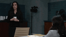 a woman in a black shirt is holding a cup and talking to a woman in a white shirt