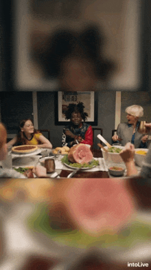 a group of people are sitting around a table with plates of food and the word intolive on the bottom right