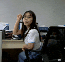 a woman wearing glasses sits at a desk